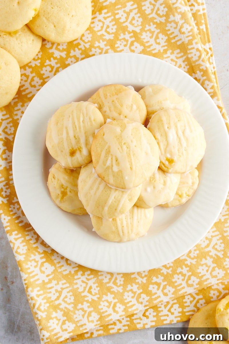 Overhead view of Pineapple Cream Cheese Cookies, perfectly baked and glazed, arranged on a white plate atop a yellow and white striped napkin