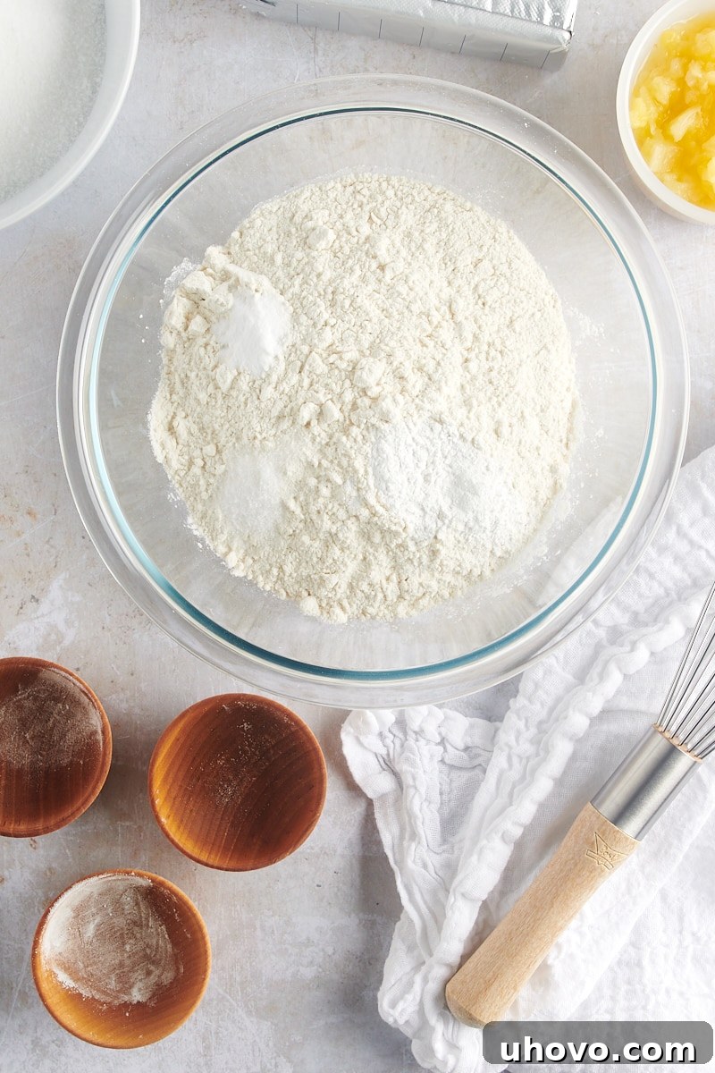 Overhead view of flour, baking powder, baking soda, and salt in a glass mixing bowl, ready to be combined