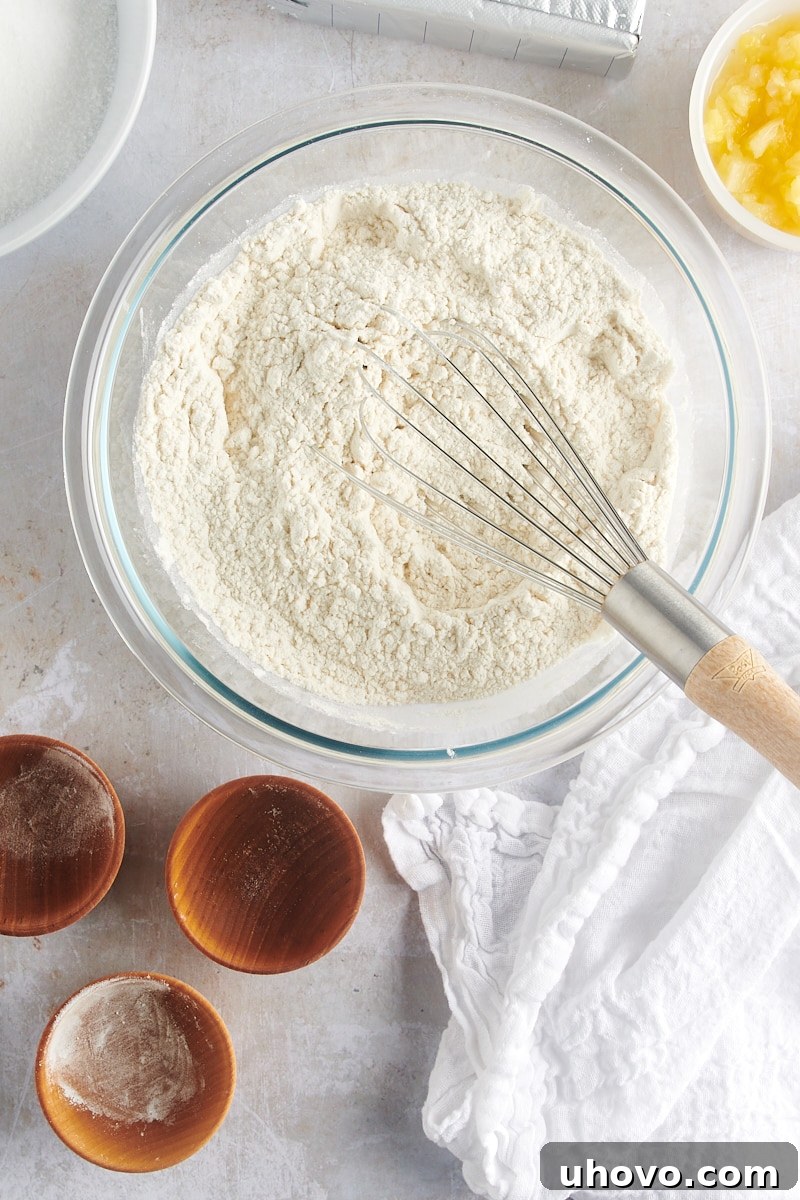 Overhead view of dry ingredients (flour, baking powder, baking soda, and salt) thoroughly mixed in a glass mixing bowl