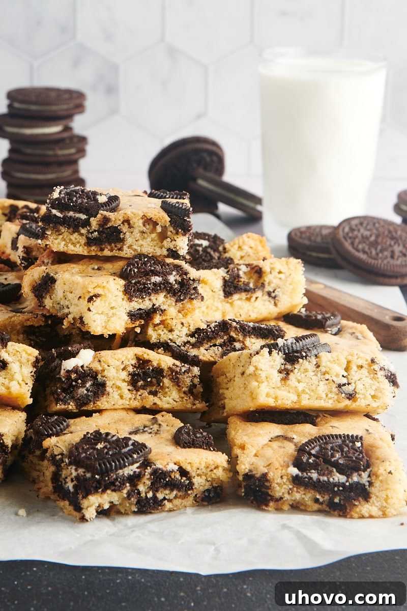 Stacks of Cookies and Cream Blondies on parchment paper, showcasing their golden brown edges and visible Oreo chunks.