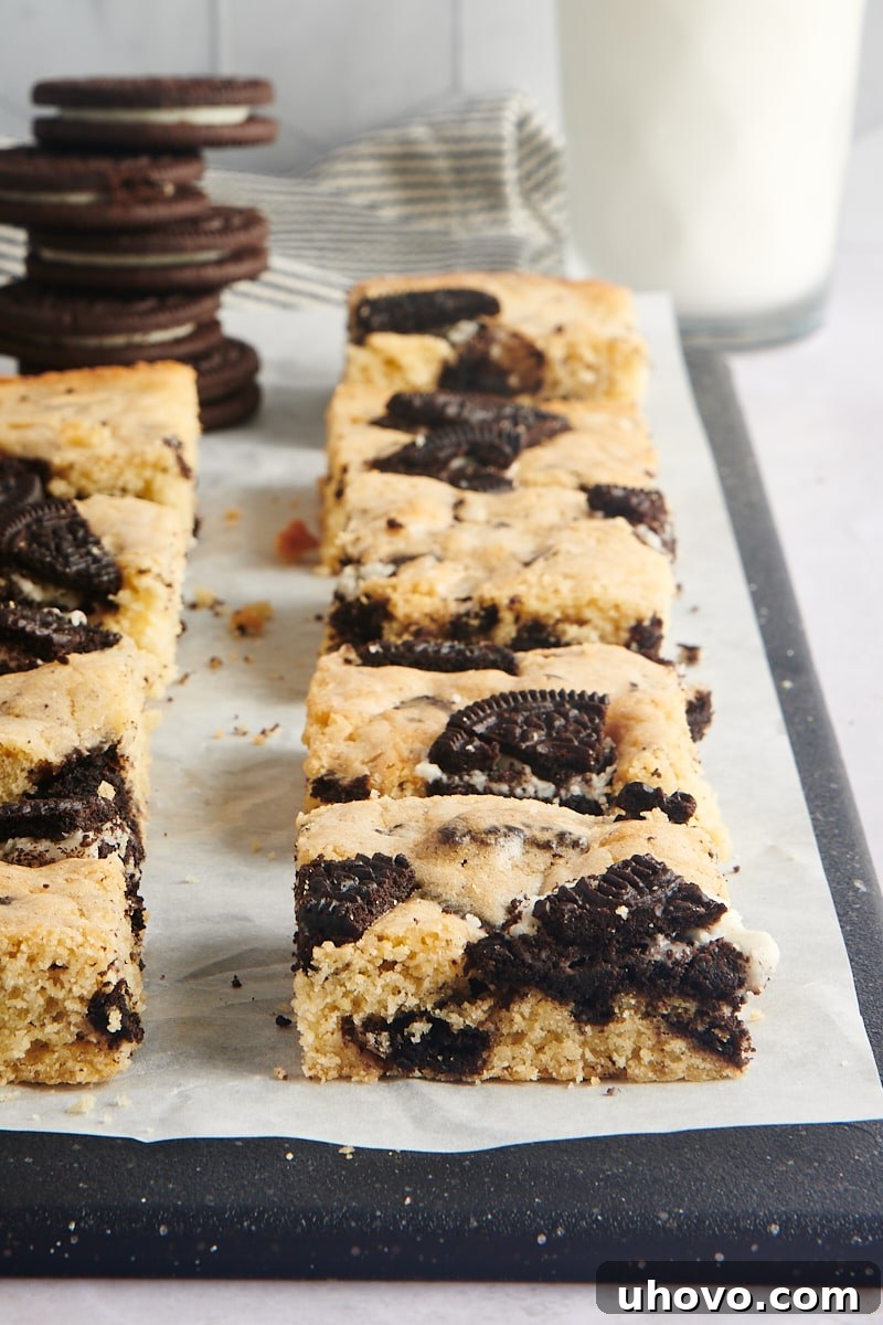 Neatly cut Cookies and Cream Blondies lined up on a cutting board, covered in parchment paper.