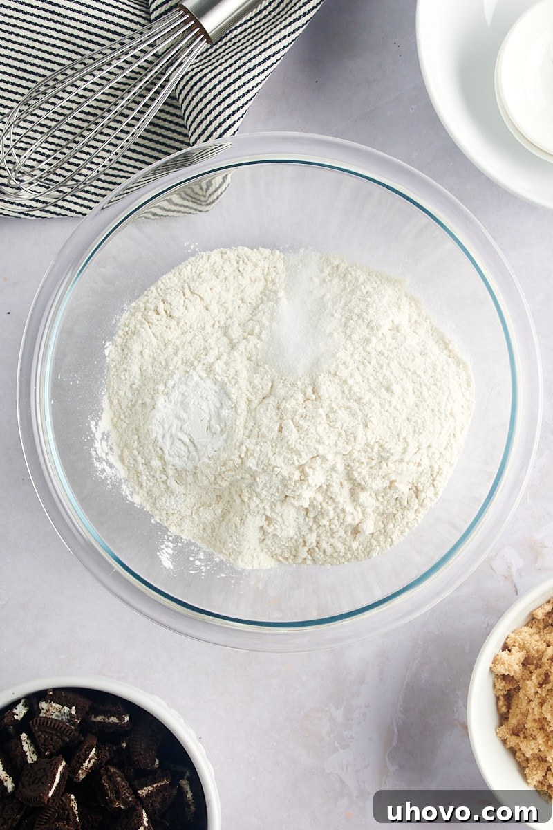Overhead view of flour, baking powder, and salt in a glass mixing bowl, ready to be combined.