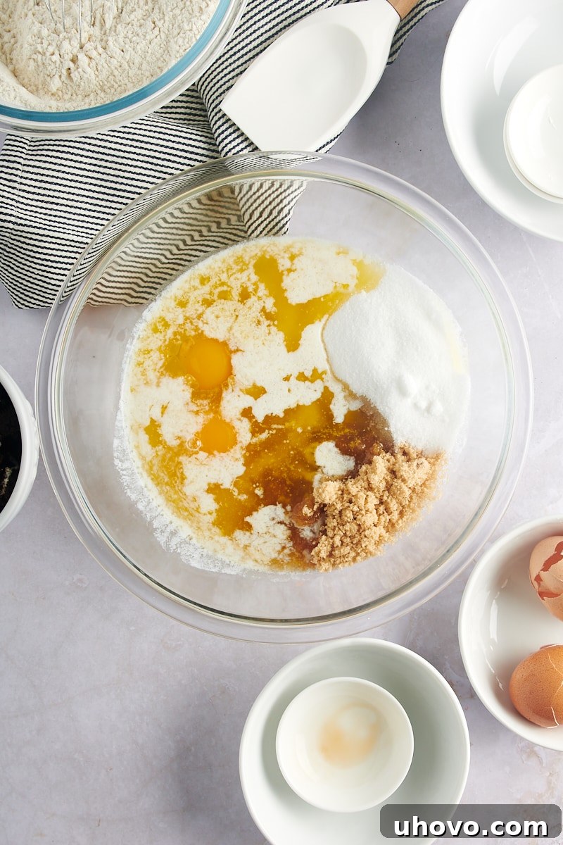 Overhead view of melted butter, brown sugar, granulated sugar, vanilla extract, and eggs in a large glass mixing bowl.