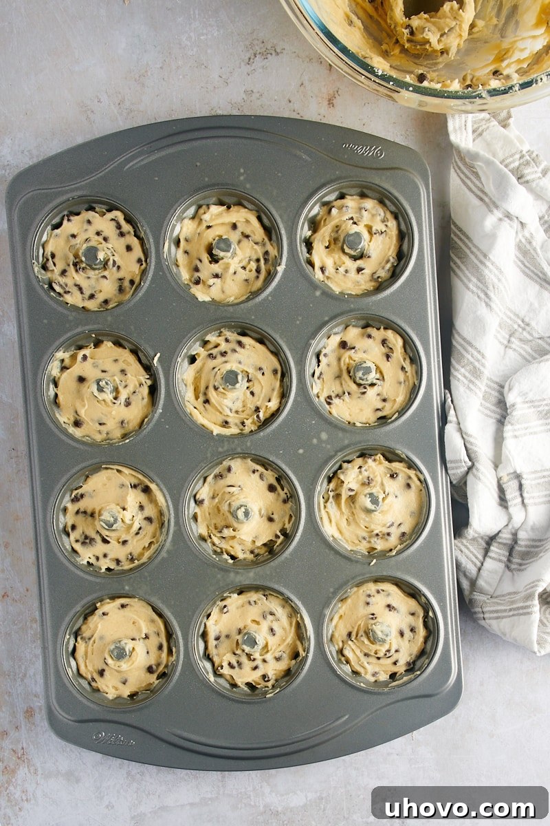 An overhead view shows chocolate chip cake batter meticulously portioned into a mini Bundt pan, ready for baking to create individual miniature cakes.