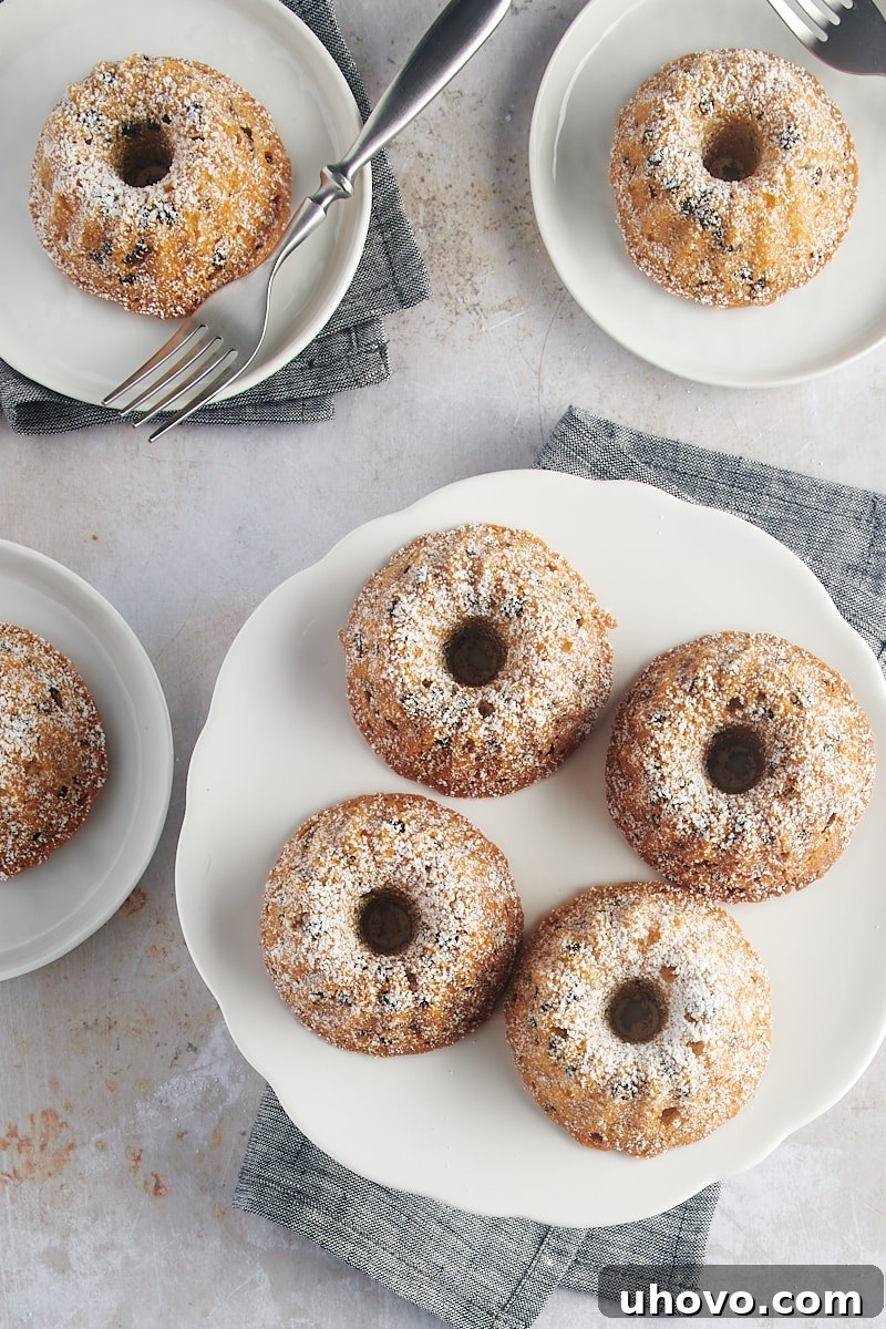 An overhead view captures a charming display of Mini Chocolate Chip Bundt Cakes on a white cake stand, accompanied by small white plates, perfect for an elegant dessert presentation.