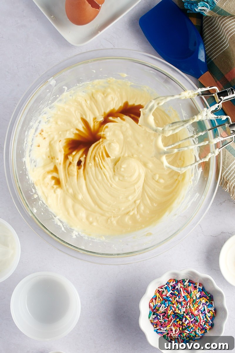An overhead view of vanilla extract being poured into the cheesecake batter in a clear glass mixing bowl, adding aromatic depth.