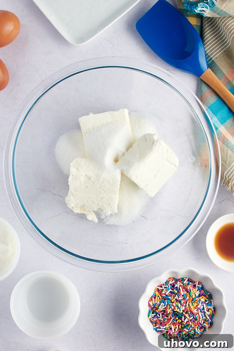 An overhead shot of cream cheese and granulated sugar waiting to be mixed in a clear glass mixing bowl.
