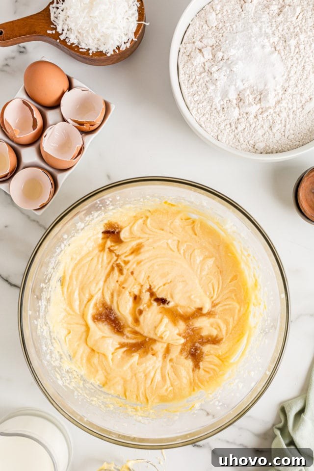 Overhead view of vanilla and almond extract being added to a bowl of creamed butter and sugar, ready to be incorporated into the cake batter.