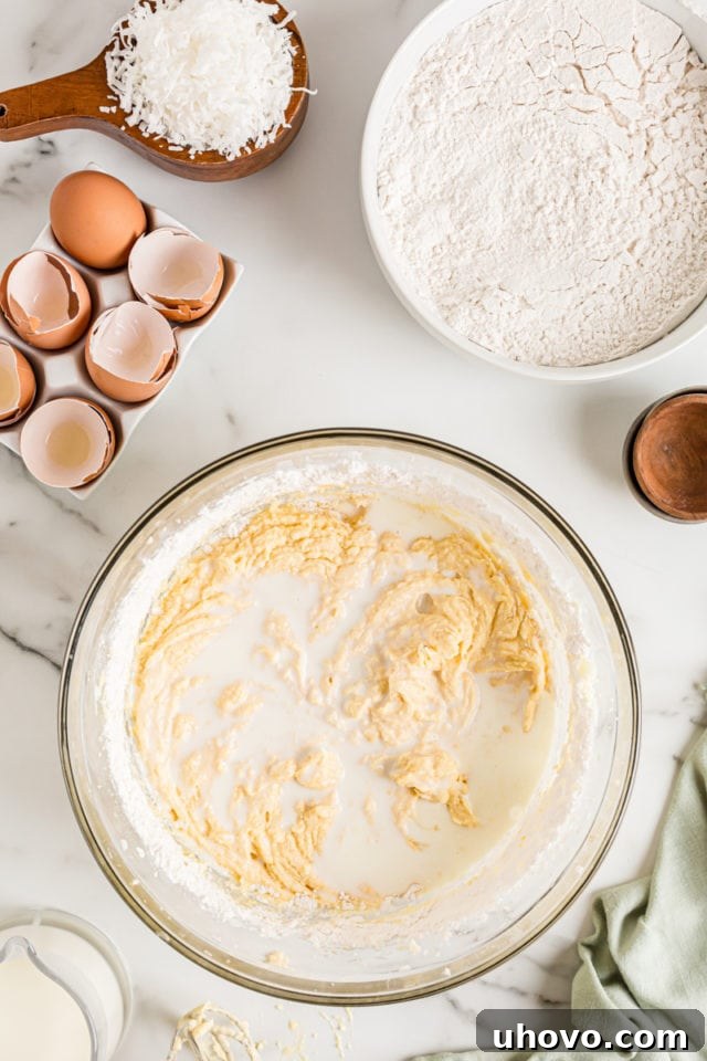Overhead view of milk being poured into a bowl of cake batter, to be alternated with dry ingredients during mixing.