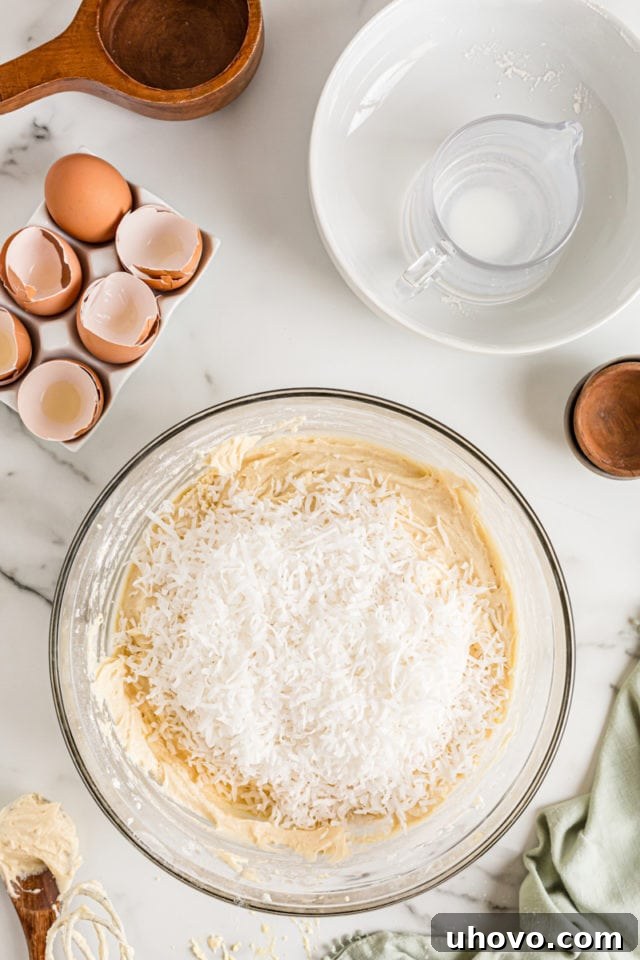 Overhead view of shredded coconut in a bowl of cake batter, waiting to be gently folded in for an even distribution.