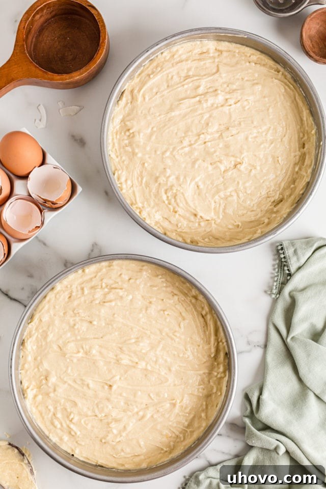 Overhead view of smooth coconut cake batter evenly divided into two greased and floured round cake pans, ready for baking.