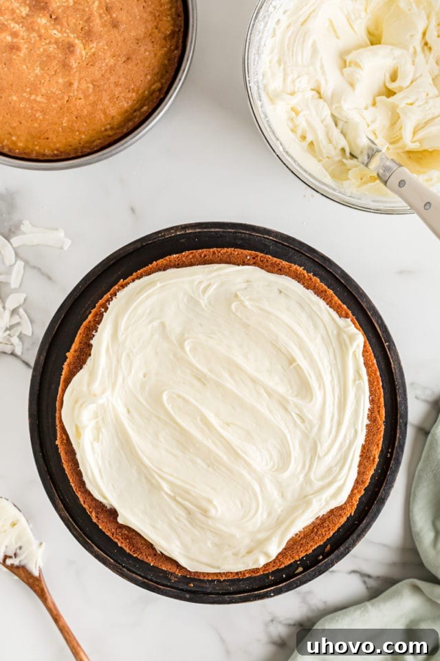Overhead view showing the first baked coconut cake layer spread with a generous amount of creamy white frosting.