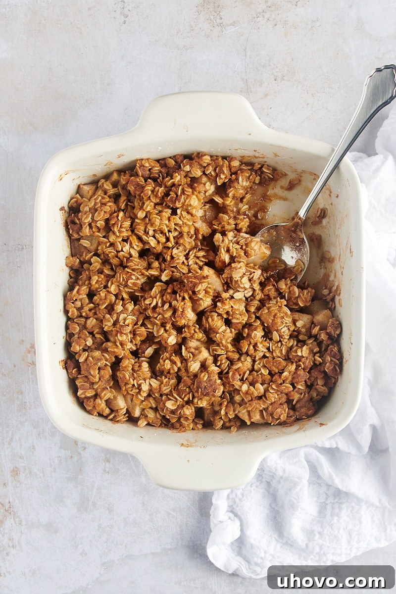 A close-up overhead view of a Brown Butter Pear Crisp in a white baking dish, with a serving spoon gently scooped into one corner, ready for serving.