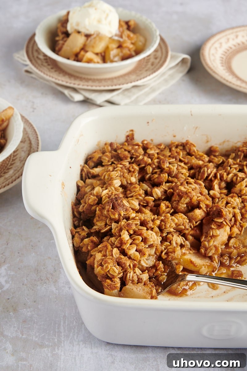 A captivating view of Brown Butter Pear Crisp in a white baking dish, with two individual servings in bowls subtly blurred in the background, hinting at shared enjoyment.