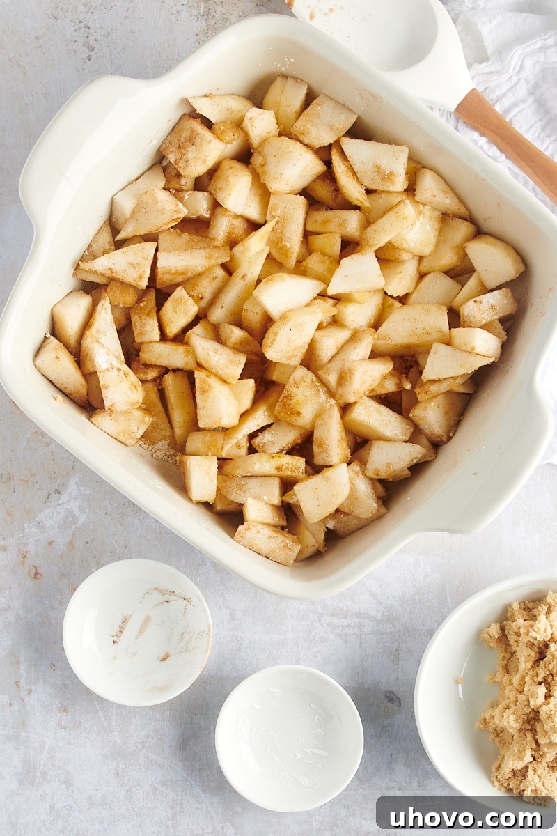 A vibrant overhead view of the mixed Brown Butter Pear Crisp filling, showcasing the glistening sliced pears coated in brown sugar and cinnamon, nestled in a white baking dish.