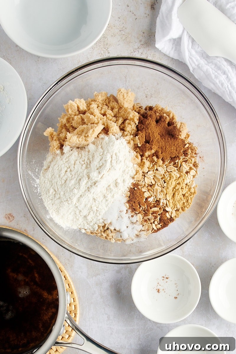 An overhead shot showcasing the crisp topping ingredients: old-fashioned oats, rich brown sugar, all-purpose flour, and a medley of aromatic spices, all waiting in a clear glass mixing bowl.