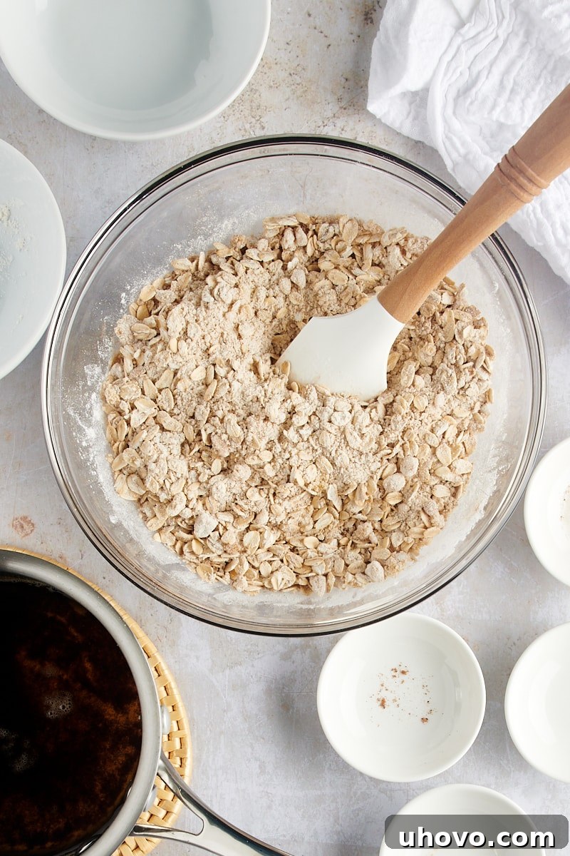 A close-up overhead view of the thoroughly mixed dry ingredients for the crisp topping, showcasing the blend of oats, brown sugar, flour, and spices in a glass mixing bowl.