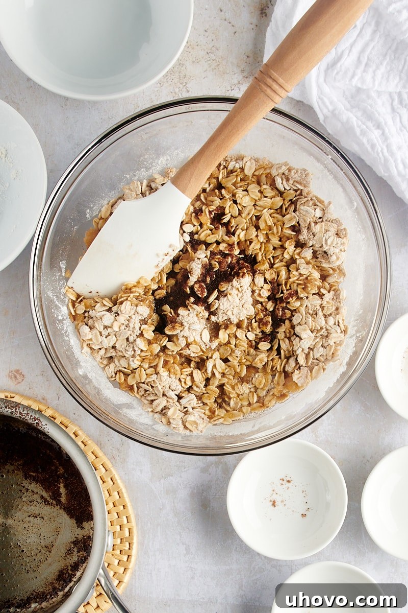 An overhead view shows the golden brown butter being poured into the oat and spice mixture for the Brown Butter Pear Crisp, beginning the transformation into a crumbly topping.