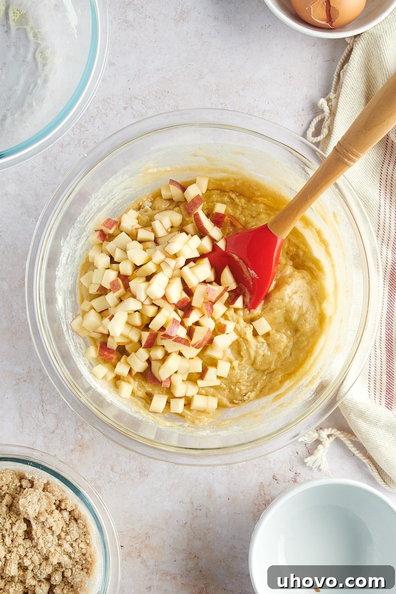 overhead view of apples added to muffin batter in a glass mixing bowl