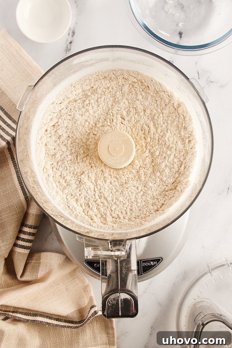 Overhead view of dry ingredients for pie crust, including flour, sugar, and salt, perfectly combined in a food processor after a few pulses.