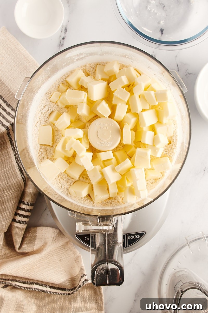 Overhead view of cold, cubed butter added to the dry pie crust ingredients in a food processor, ready for pulsing.