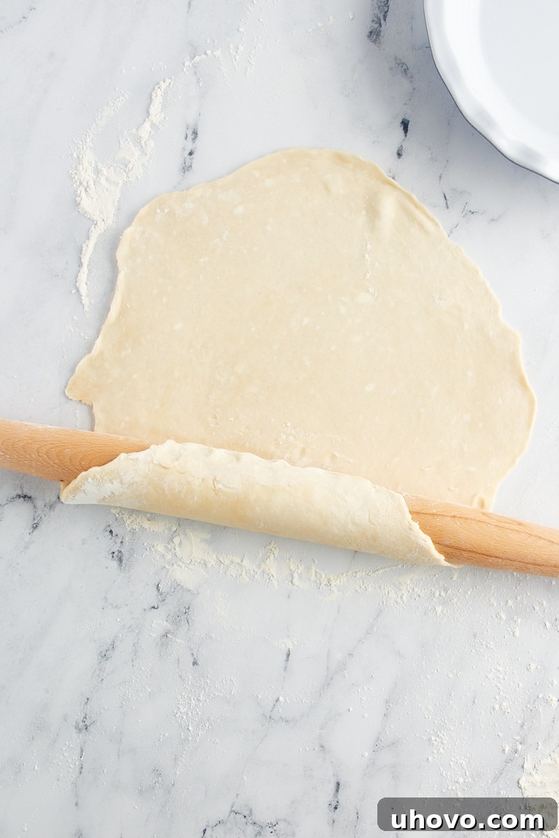 Overhead view of a perfectly rolled pie crust gently being draped over a wooden rolling pin, ready for the transfer to a pie pan.