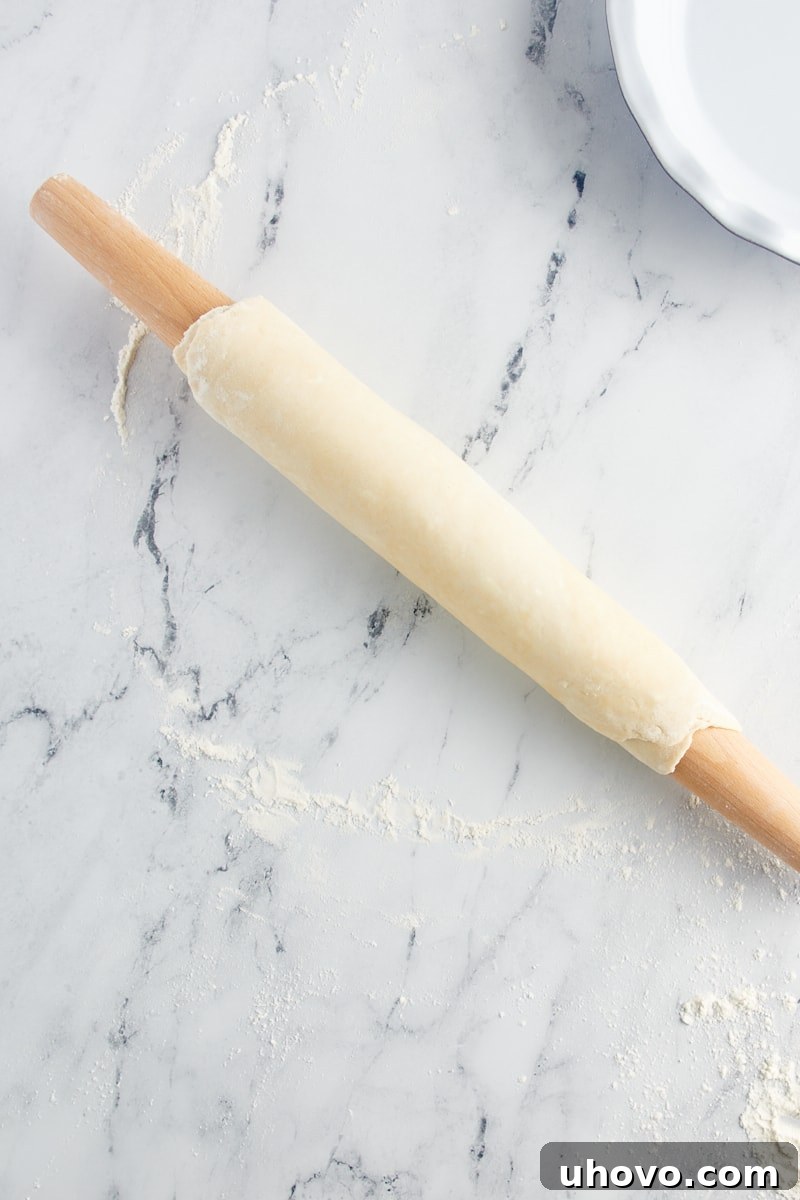 Overhead view of a pie crust fully wrapped around a wooden rolling pin, providing a secure and easy way to lift and transfer the delicate dough.