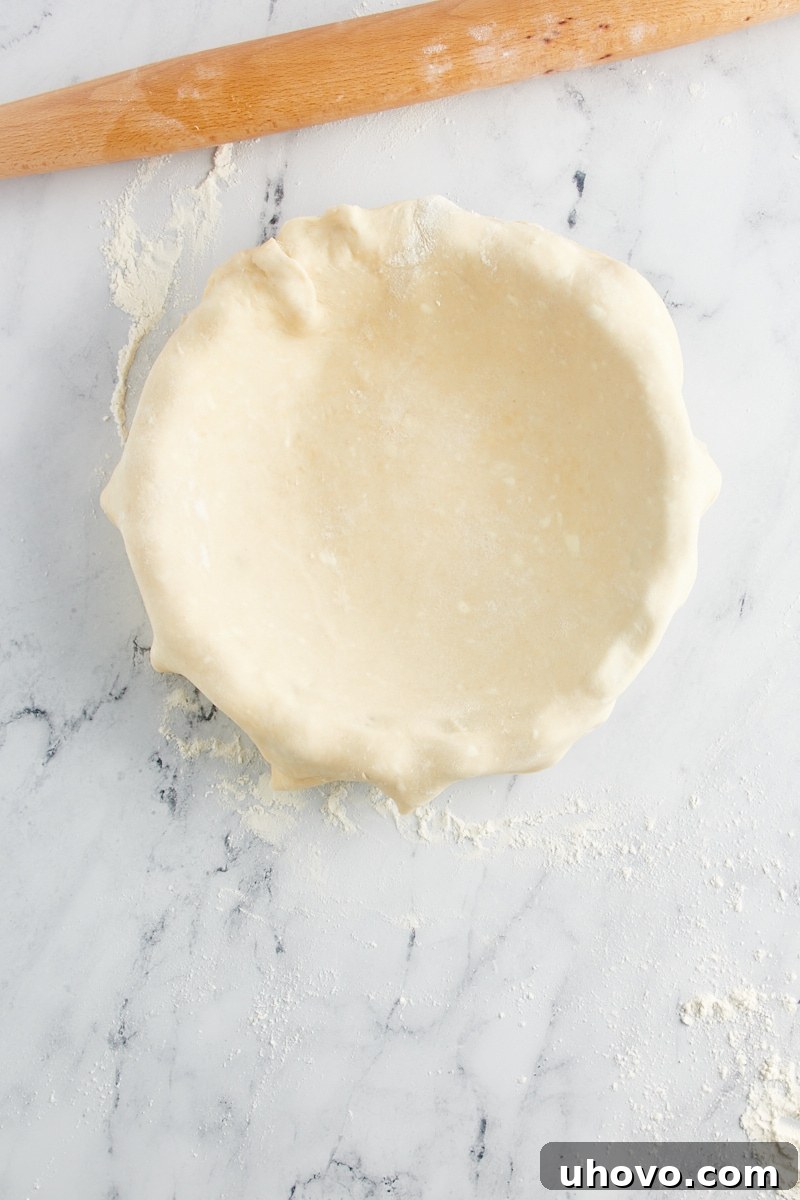 Overhead view of pie crust dough gently pressed into a pie plate, showcasing proper fitting without stretching, ready for trimming and decorating.