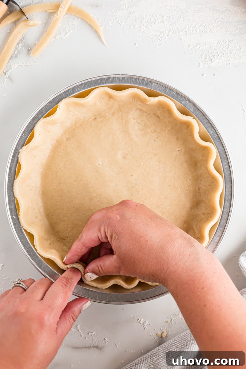 Close-up of a hand creating a classic fluted edge on a pie crust by pressing dough between thumb and forefinger, showcasing traditional pie finishing.