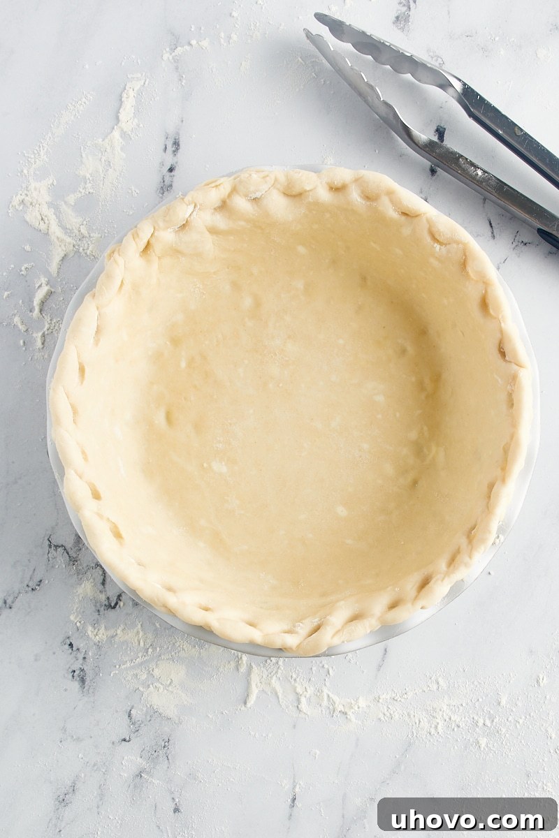 Close-up of a decorative pie crust edge intricately crimped using kitchen tongs, creating a unique and visually appealing textured pattern.