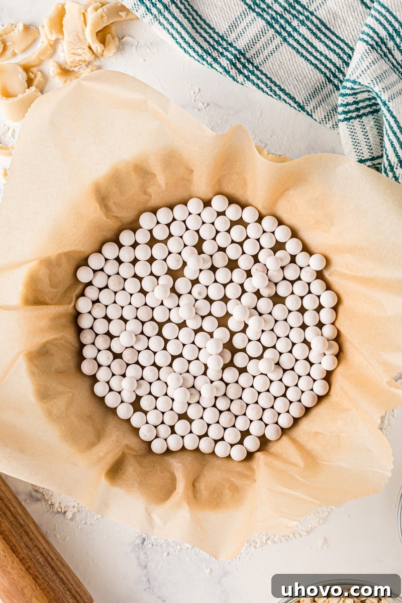 Overhead view of a pie crust lined with parchment paper and filled with ceramic pie weights, demonstrating the proper setup for blind baking to prevent shrinkage and bubbling.
