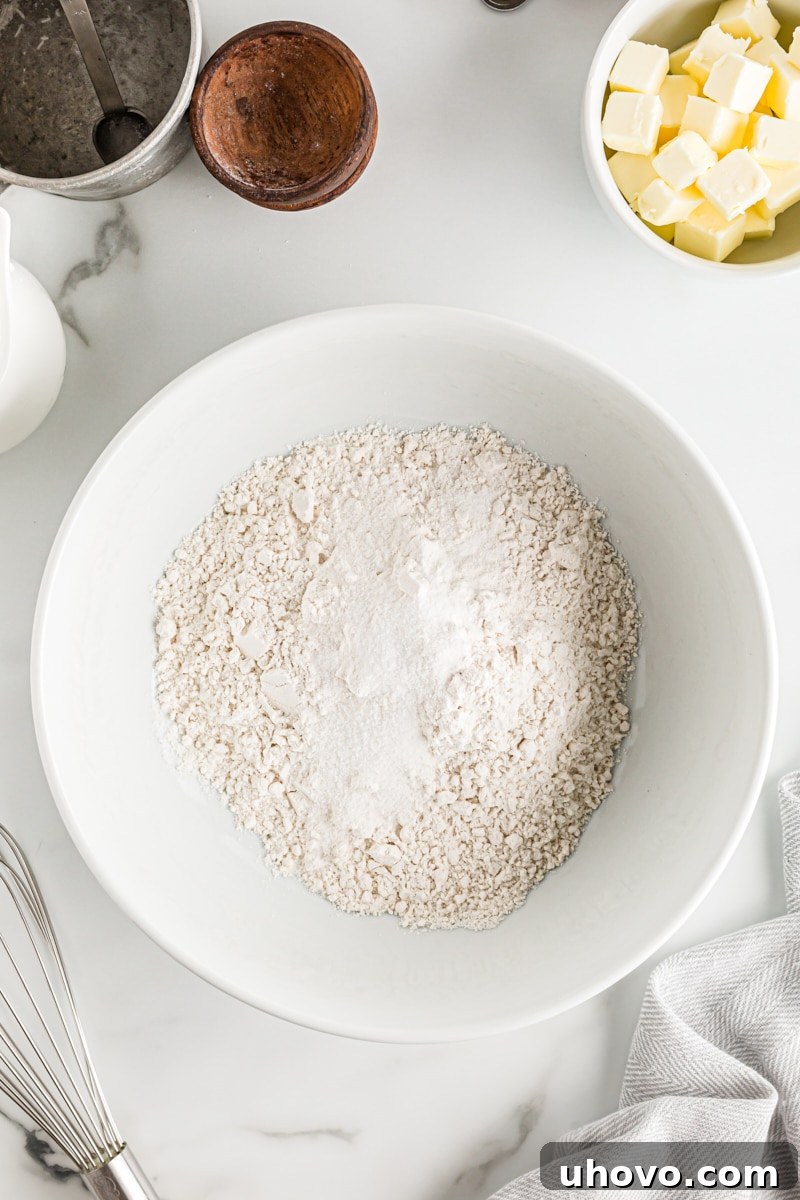 Overhead view of all-purpose flour, granulated sugar, and salt perfectly mixed together in a white ceramic mixing bowl, ready for the next step of pie crust preparation.