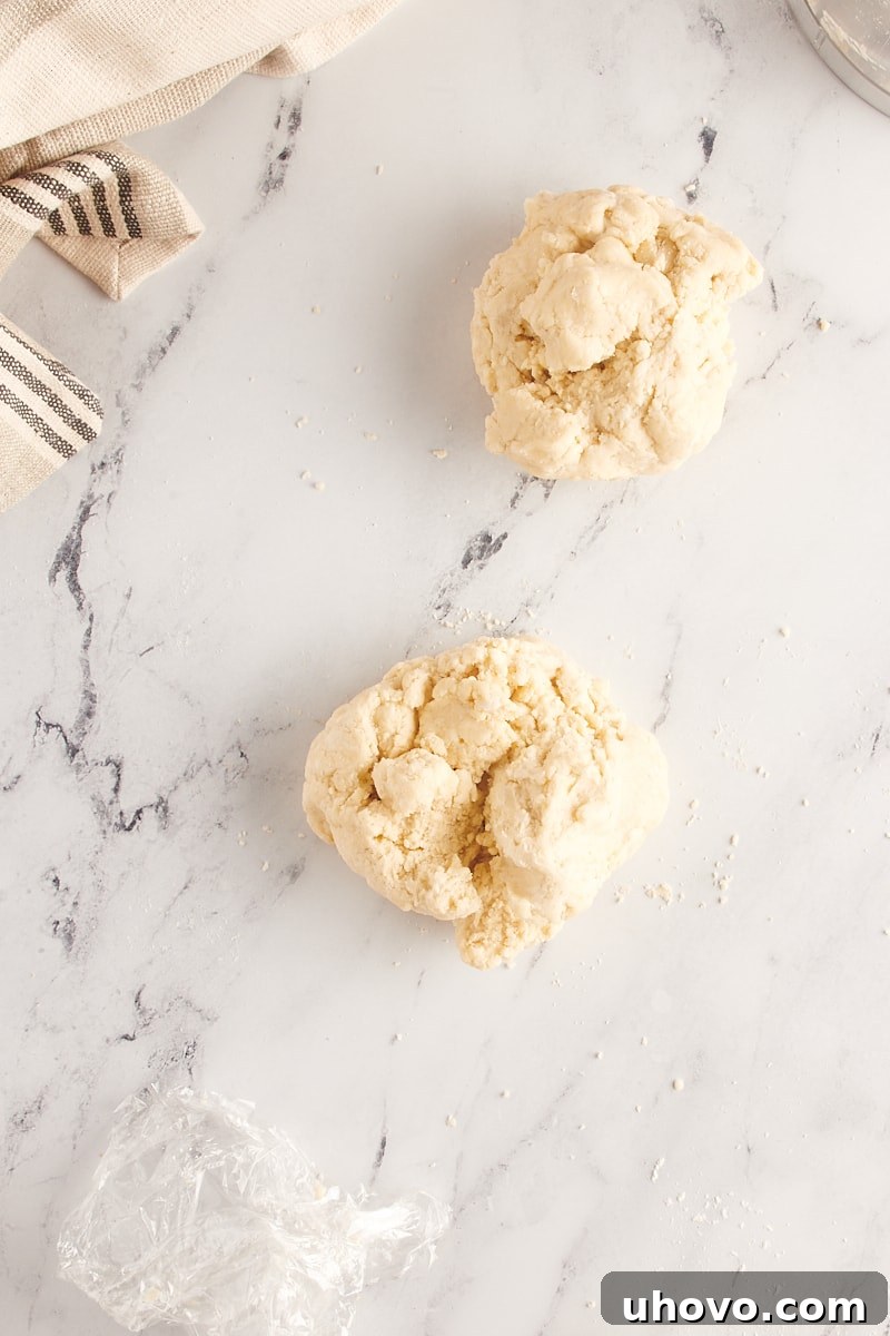 Overhead view of pie crust dough gently divided into two equal portions in a white mixing bowl, ready to be shaped into discs and chilled.
