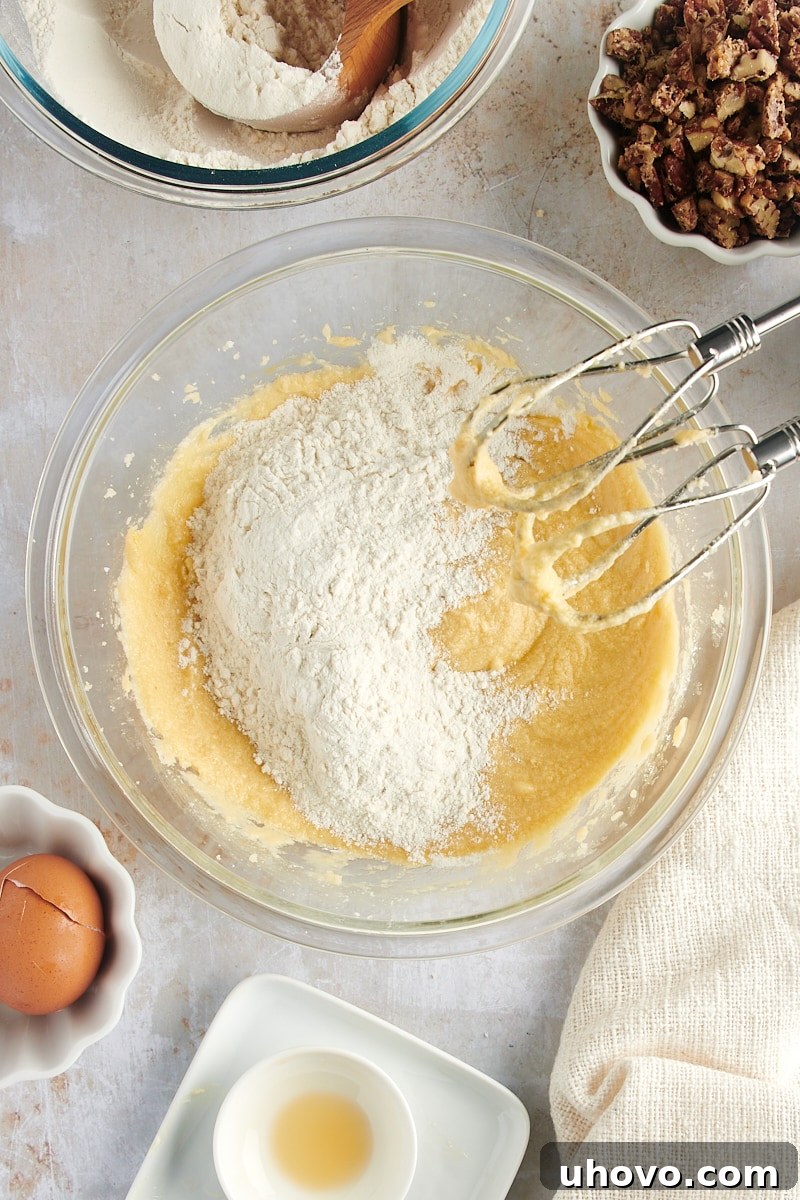 Overhead view of dry ingredients gradually added to the wet mixture for Maple Pecan Cookies, minimizing overmixing.