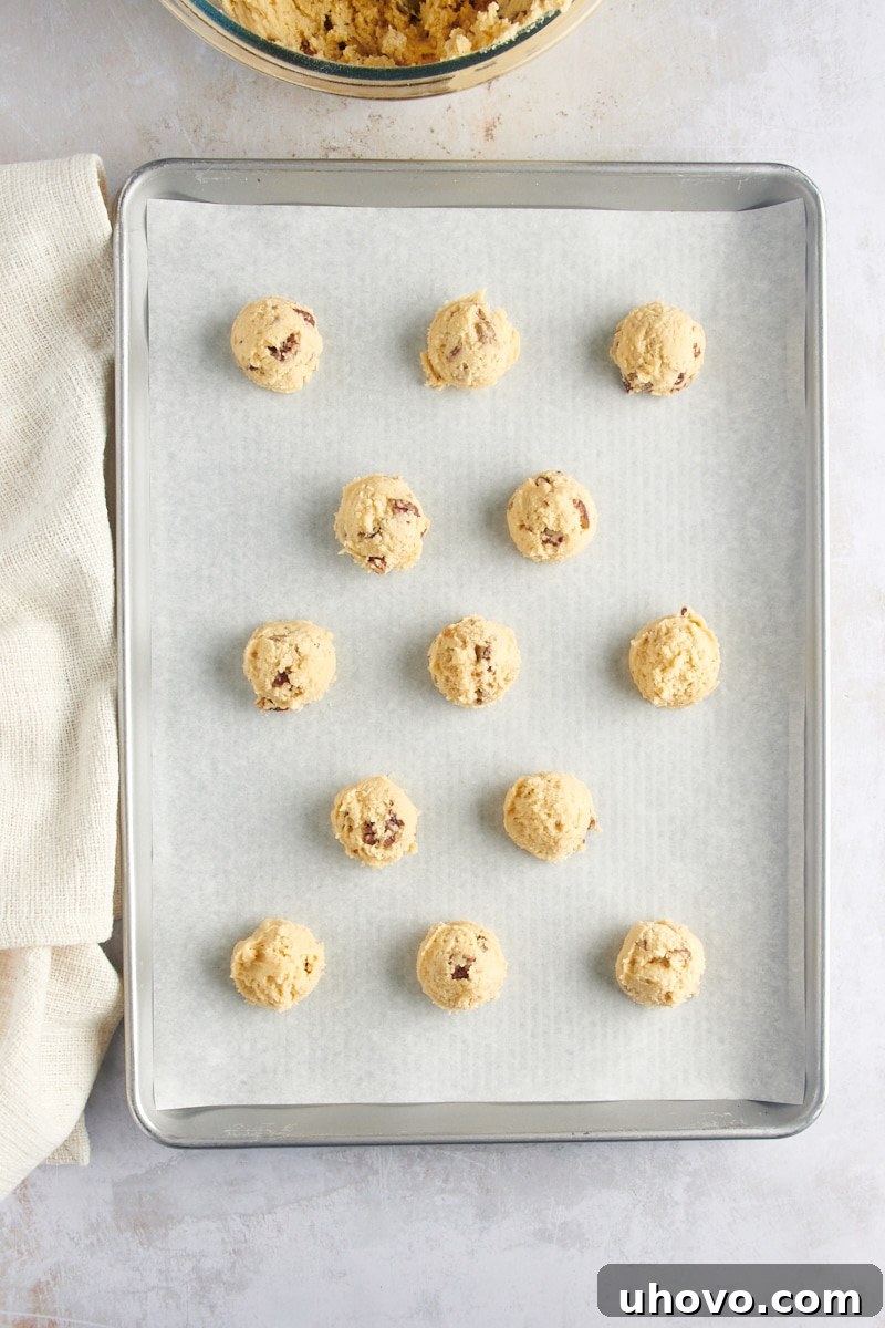 Overhead view of perfectly scooped Maple Pecan Cookie dough balls arranged on a parchment-lined baking sheet, ready for topping.