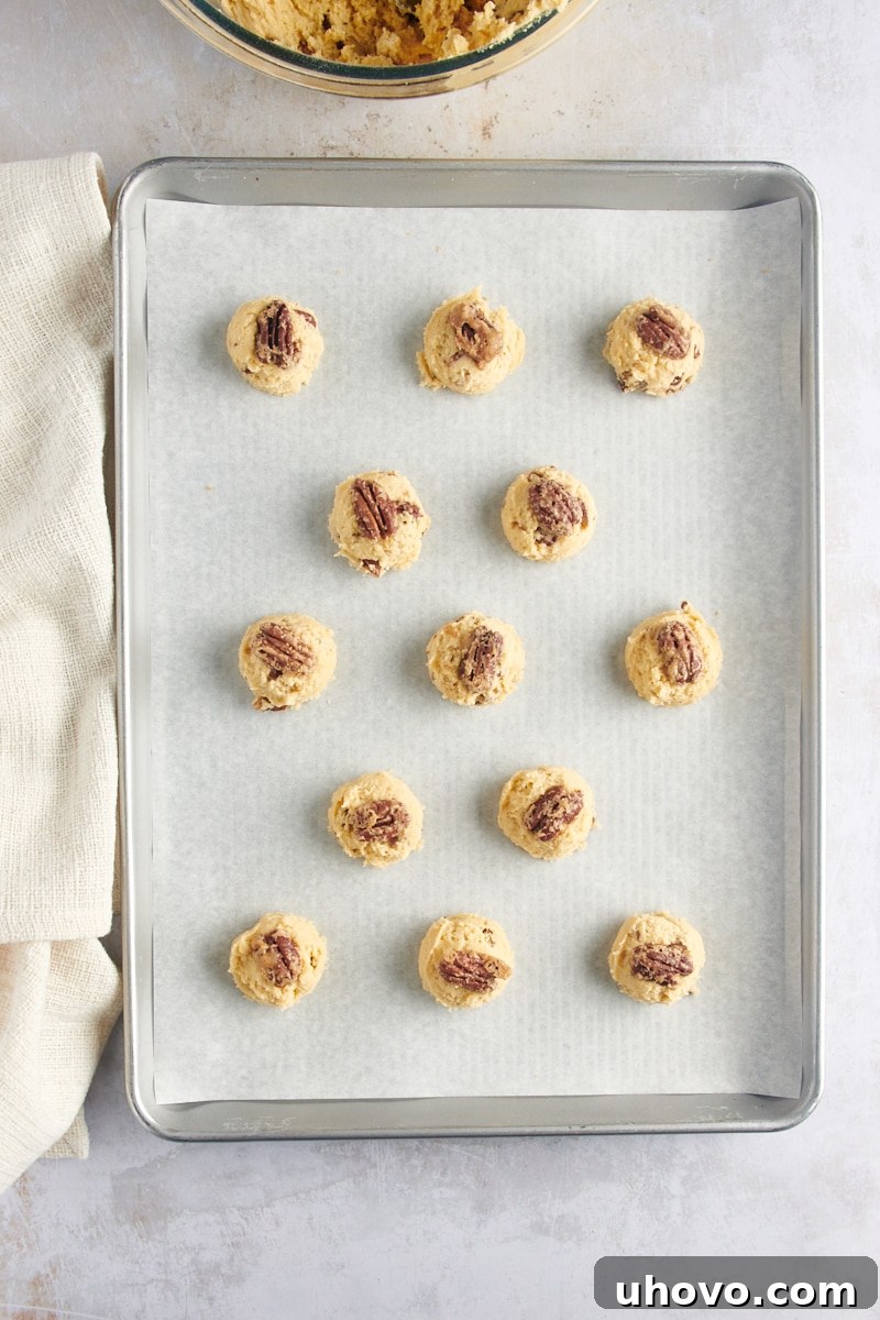 Overhead view of Maple Pecan Cookie dough balls topped with elegant pecan halves, ready for baking.