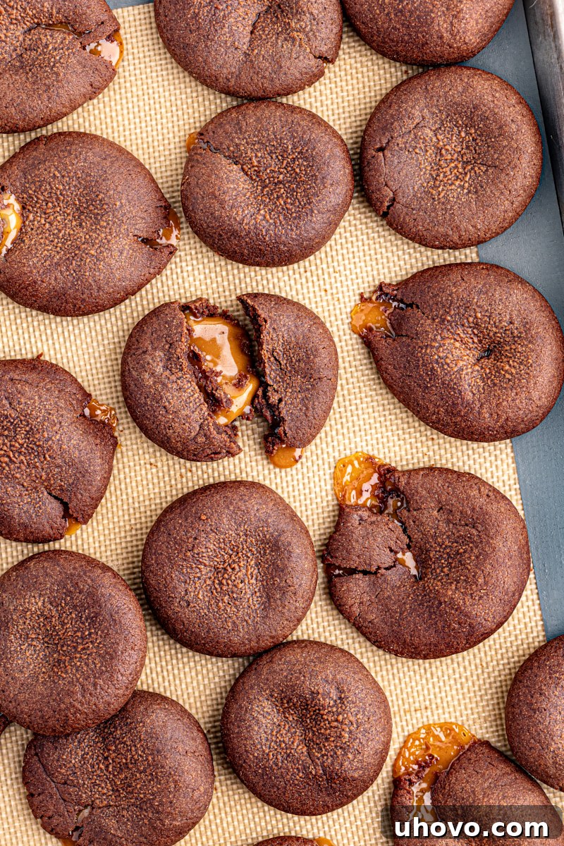 Overhead view of chocolate caramel cookies on silpat with some broken to show gooey middles