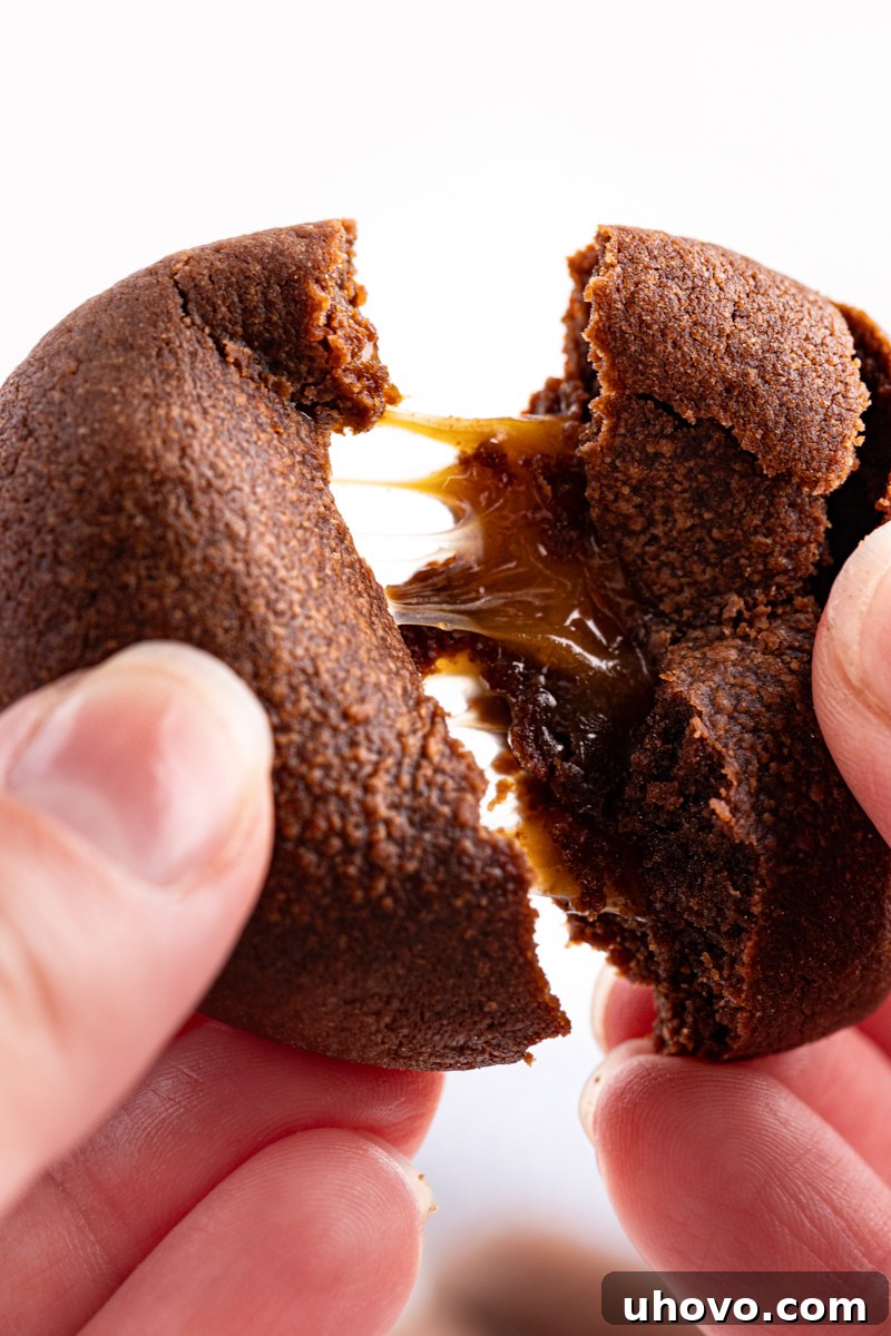 Hand breaking apart chocolate caramel cookie to show gooey center