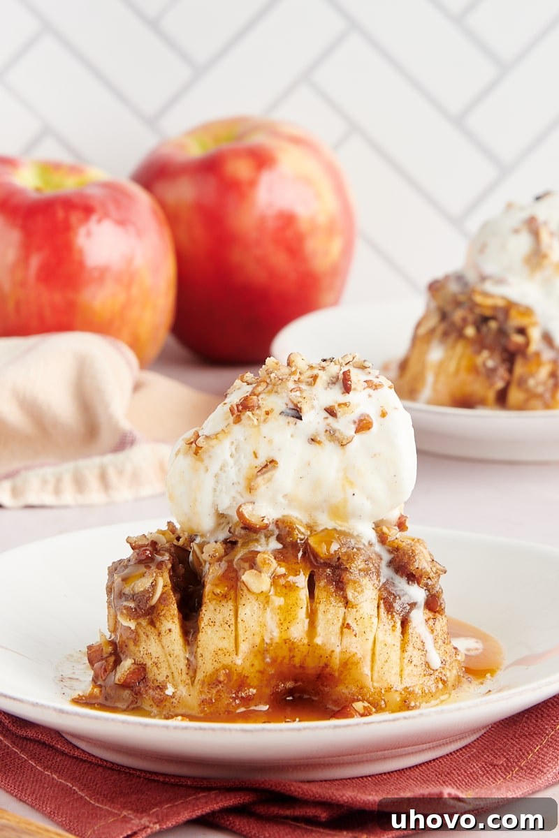 A baked hasselback apple topped with a scoop of vanilla ice cream, drizzled with caramel sauce, and sprinkled with chopped nuts, presented on a white plate