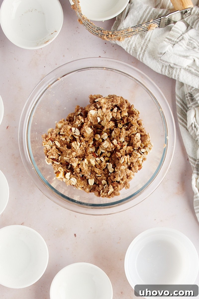 Overhead view of the fully mixed crumb topping for baked hasselback apples in a glass bowl, showing a combination of butter, flour, spices, nuts, and oats