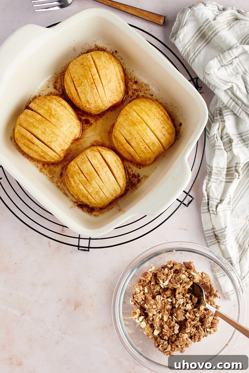 Overhead view of partially baked hasselback apples in a white baking dish, still uncovered, after the initial baking phase