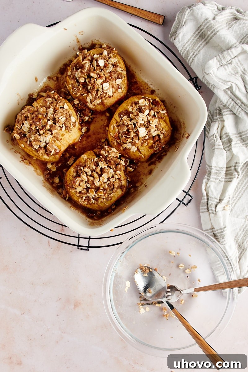 Overhead view of hasselback apples generously topped with the crumb mixture, featuring oats, nuts, and spices, resting in a white baking dish before final baking
