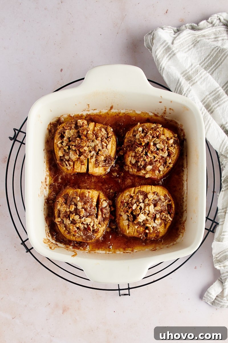 Overhead view of freshly baked hasselback apples in a white baking dish, placed on a wire cooling rack to rest