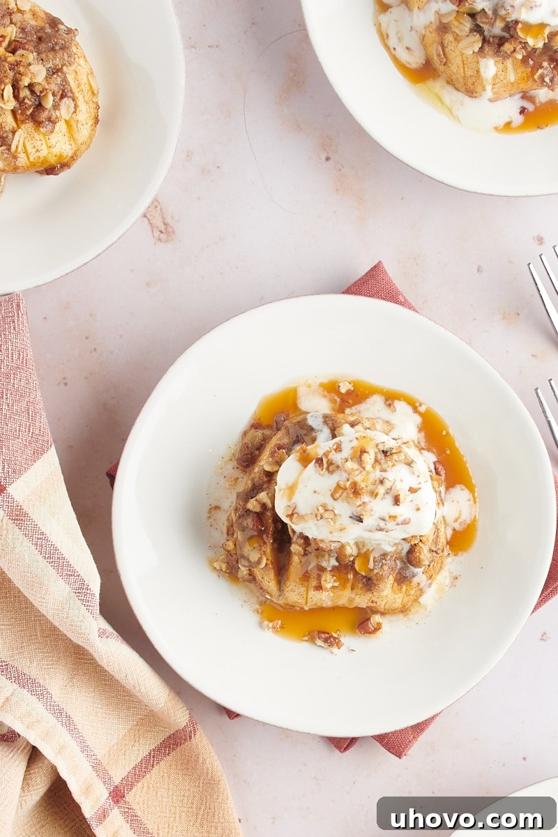 Overhead view of a single baked hasselback apple topped with a scoop of vanilla ice cream, generous drizzles of caramel sauce, and a sprinkle of chopped nuts, served on a white plate