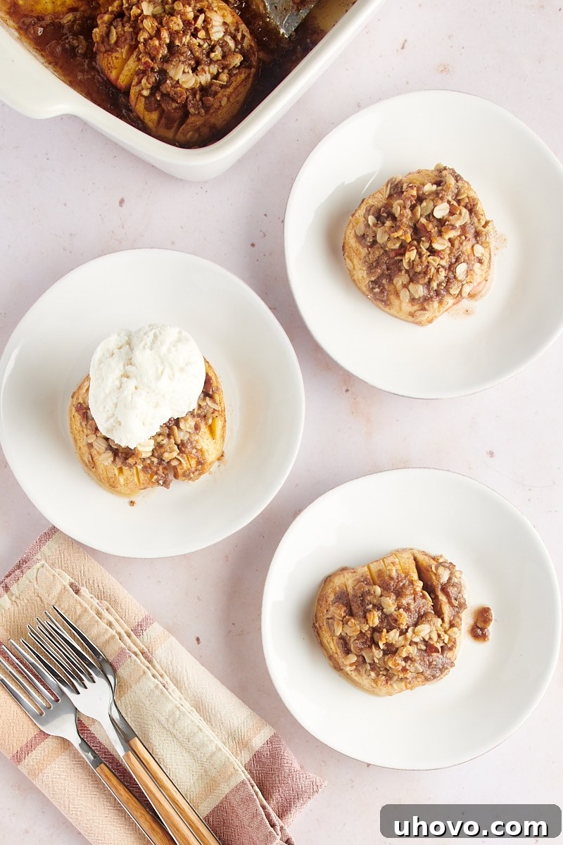 Overhead view of three white plates, each holding a baked hasselback apple garnished with a sprig of mint