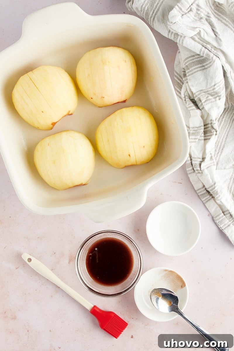 Overhead view of four peeled, halved, and cored apples arranged in a white baking dish, ready for slicing
