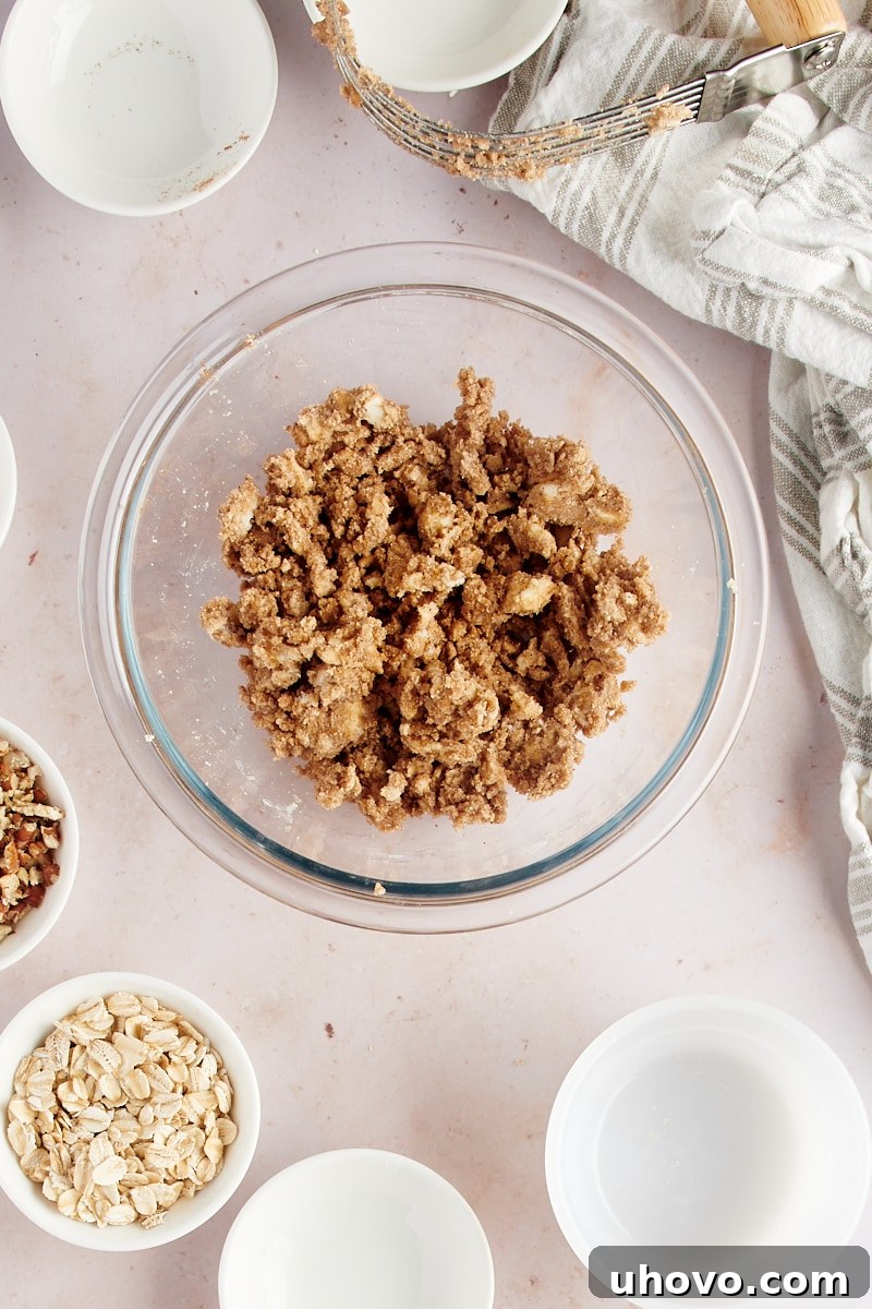 Overhead view of a partially mixed topping for baked apples in a glass bowl, showing butter, flour, and spices combined into coarse crumbs