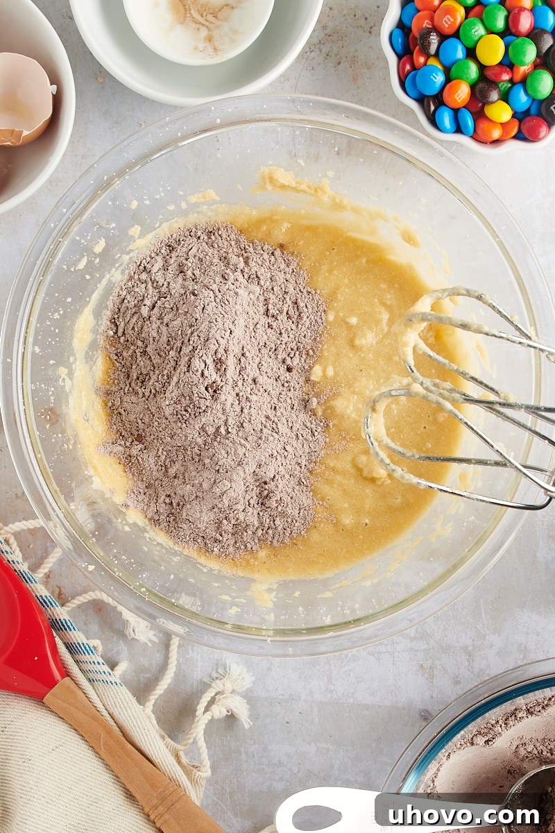 Overhead view of dry ingredients being gradually added to the wet mixture to form chocolate cookie dough.