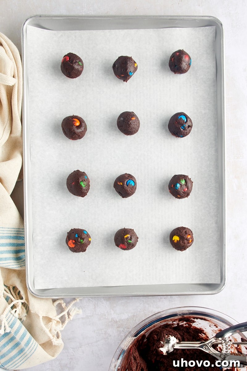 Overhead view of perfectly portioned Chocolate M&M Cookie dough balls arranged on a parchment-lined baking sheet, ready for the oven.