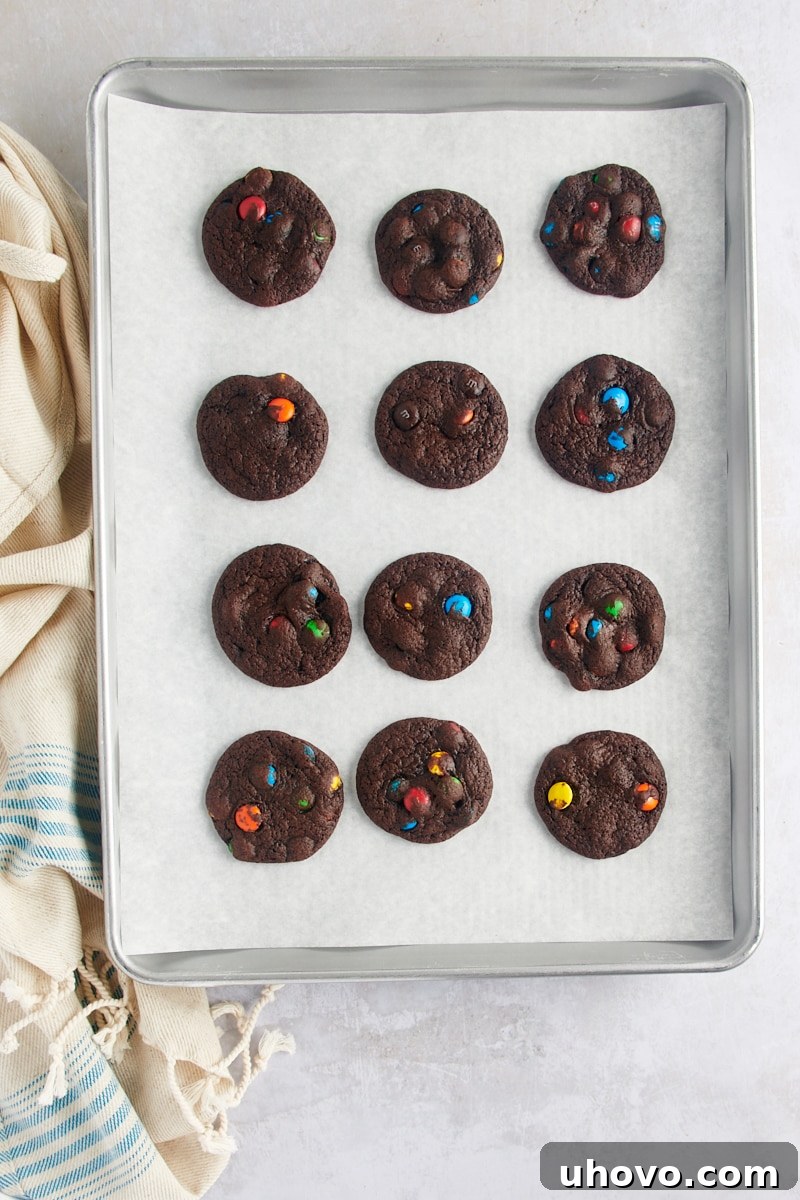 Overhead view of freshly baked Chocolate M&M Cookies cooling on a parchment-lined baking sheet, placed on a wire rack.